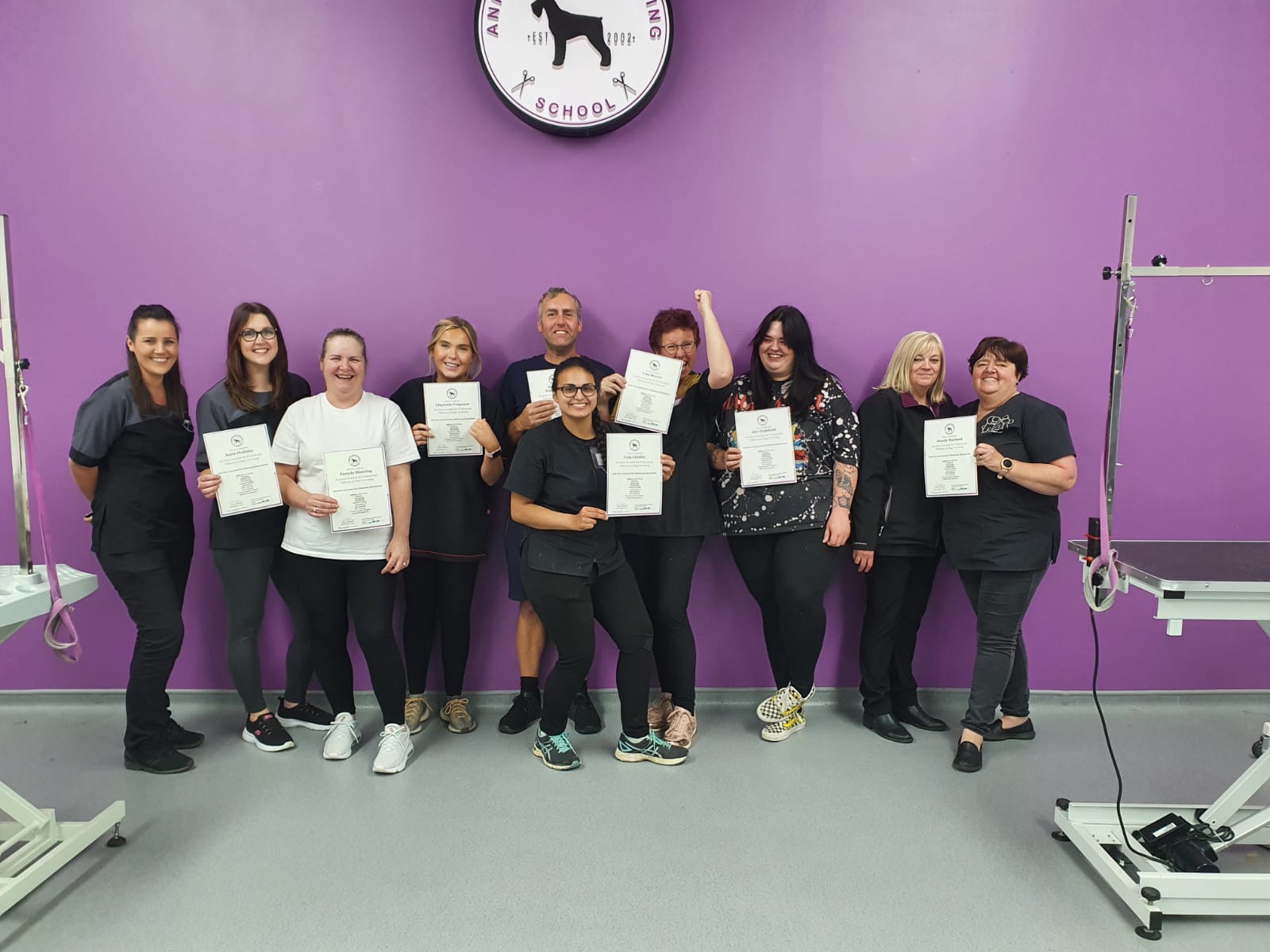 A class of Anrich students in grooming uniforms with their certificates in the training room
